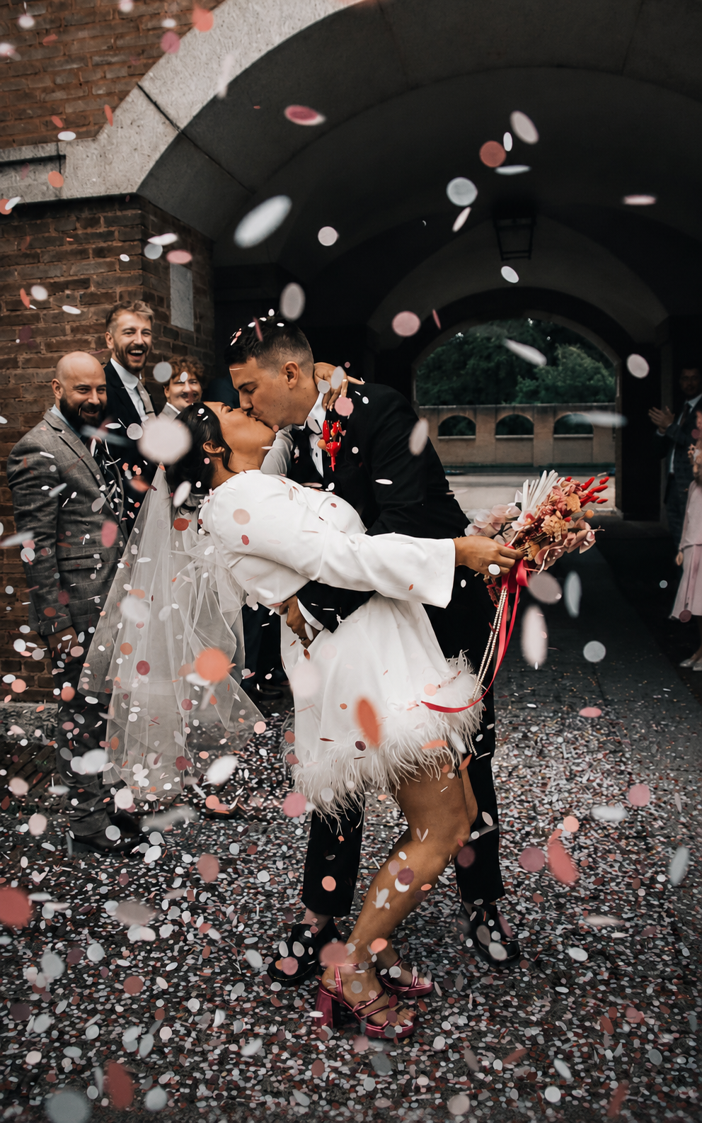Couple kissing in colour confetti shower, wedding